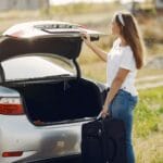 Uśmiechnięta turystka wkłada walizkę do bagażnika auta przed wyjazdem