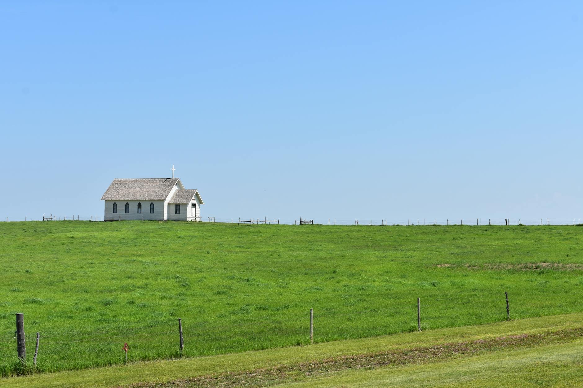 Samotna wiejska kaplica pośród zielonego pola pod błękitnym niebem