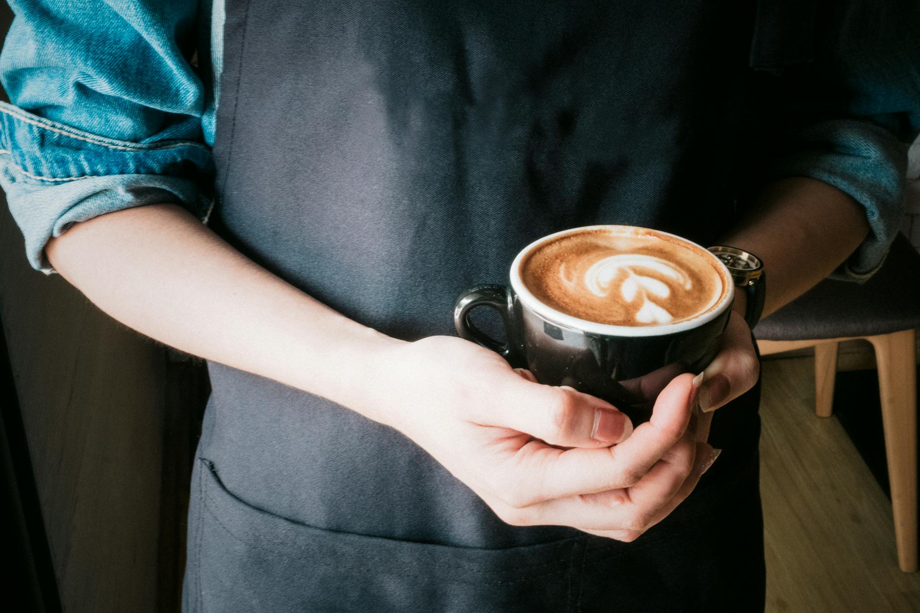 Barista trzyma filiżankę kawy z latte art w przytulnej kawiarni w Lanckoronie Barista trzyma filiżankę kawy z latte art w przytulnej kawiarni w Lanckoronie